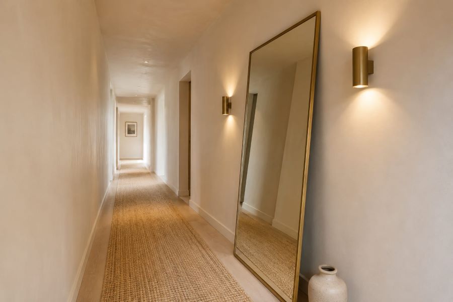 Full length mirror and brass sconces in narrow beige hallway
